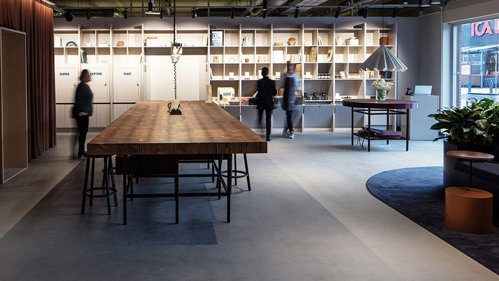 Ett showroom med ett stort bord, en hylla längs med helvägg, tre människor i bakgrunden.